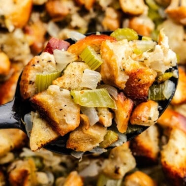 A close up view of a spoon of homemade stuffing being dished out of th epan.