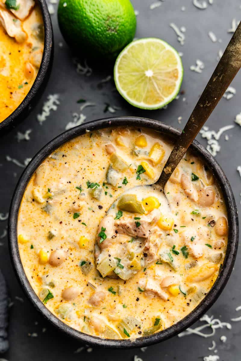 An overhead view of a black bowl full of white chicken chili with a spoon resting in the middle.