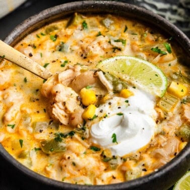 A close up view of a bowl of white chicken chili topped with a dollop of sour cream.