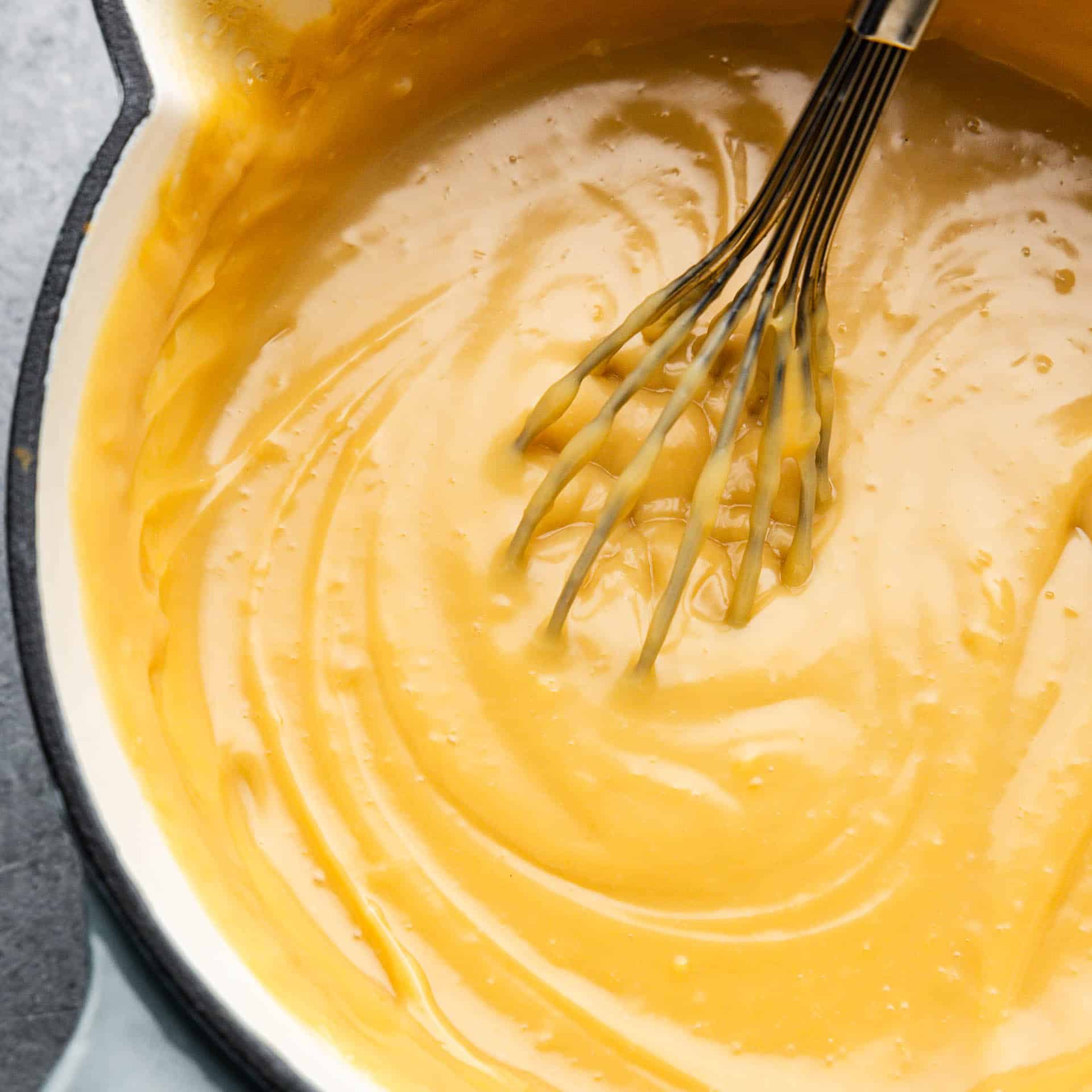 An overhead look into a pan of warm homemade butterscotch pudding with a whisk sticking out.