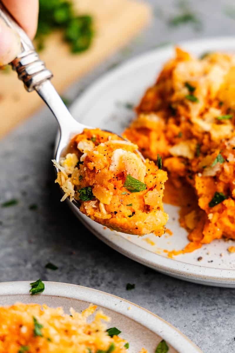 A close up of a spoon lifting a bite of cheesy carrot casserole from a plate.