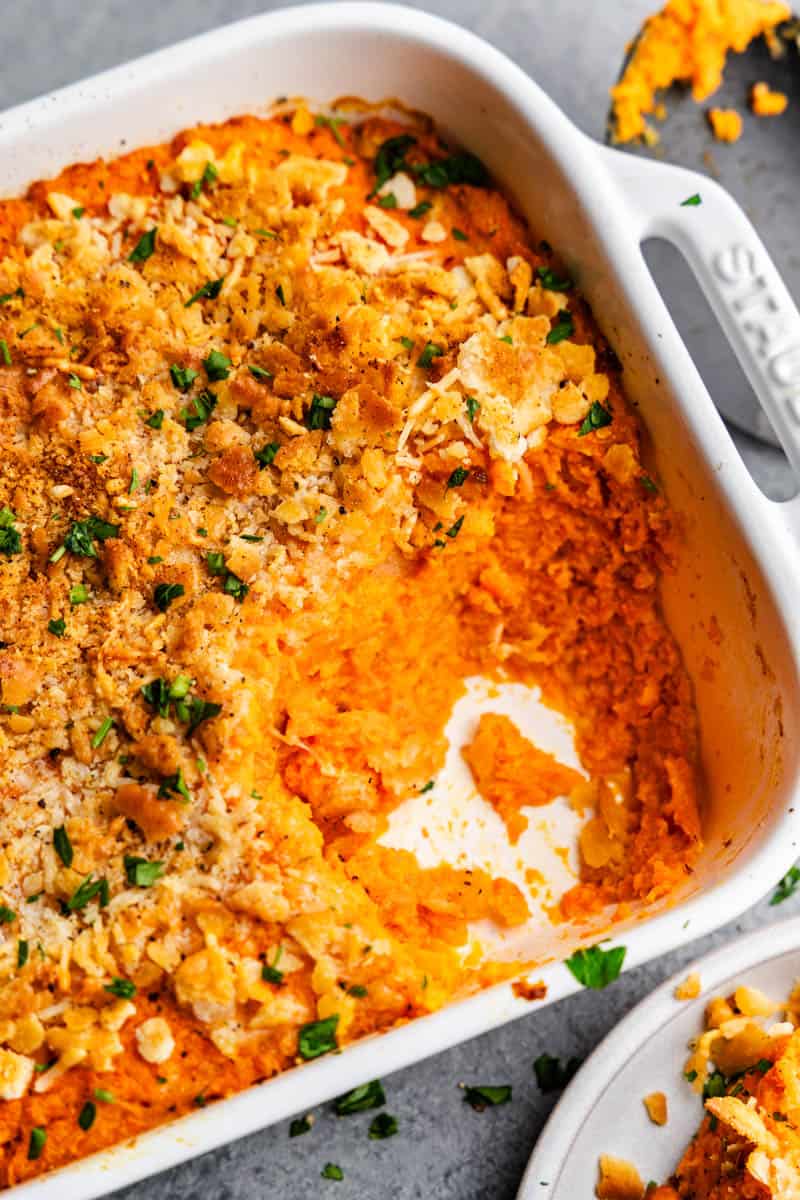 A close up of a casserole dish filled with crispy baked cheesy carrot casserole with the bottom corner portion already scooped out of the dish.