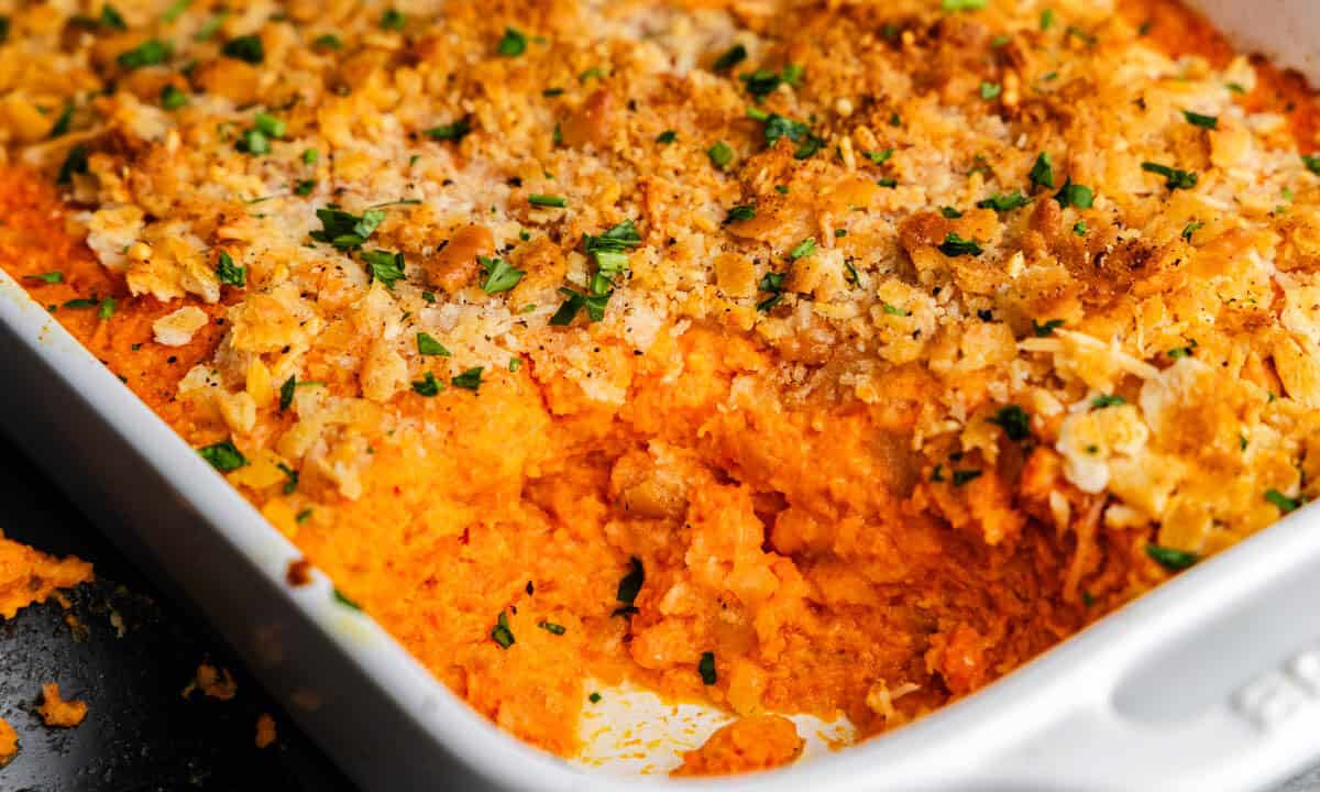 A close up of the corner of a white casserole dish filled with cheesy carrot casserole, with the corner portion already having been served.