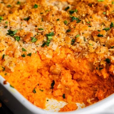 A close up of the corner of a white casserole dish filled with cheesy carrot casserole, with the corner portion already having been served.