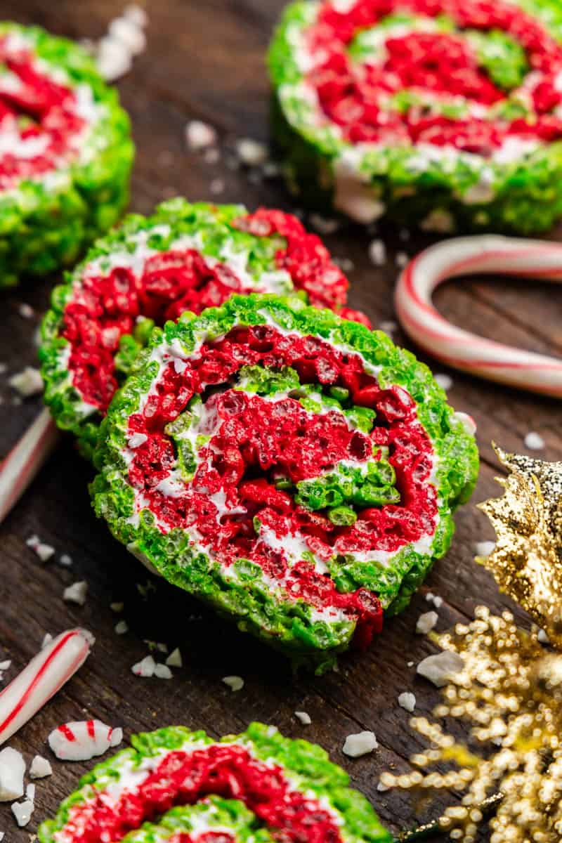 Two slices of Christmas rice krispie treat pinwheels, with layers of red, green, and white swirled together. Candy canes are on the side.