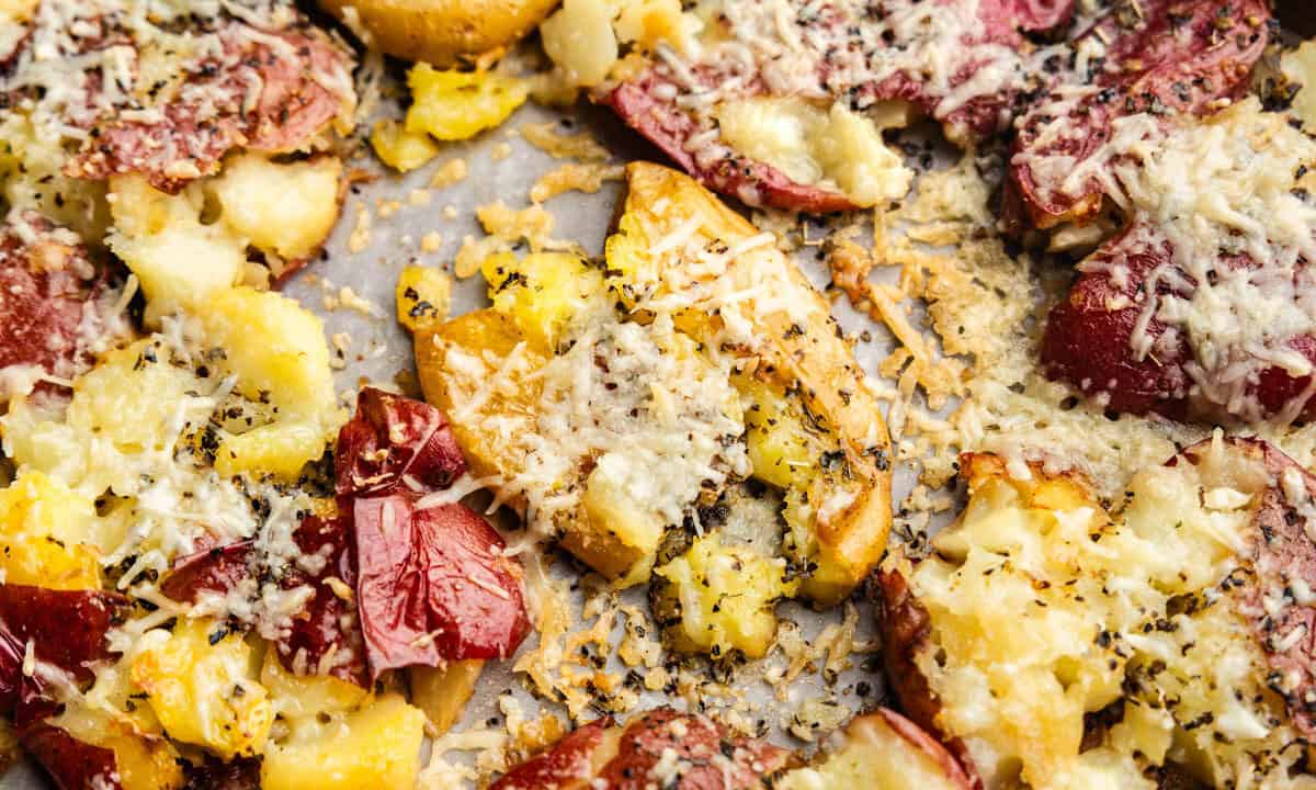 A close up of a sheet pan holding smashed red potatoes baked to a golden brown with parmesan cheese and garlic.