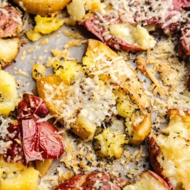 A close up of a sheet pan holding smashed red potatoes baked to a golden brown with parmesan cheese and garlic.