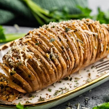 A hasselback potato on a plate with a fork resting on the edge of the plate.