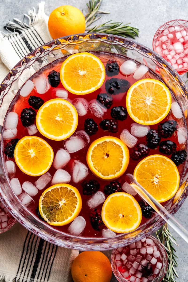 An overhead view of a punch bowl filled with holiday punch, with ice cubes, fresh blackberries and orange slices floating at the top.