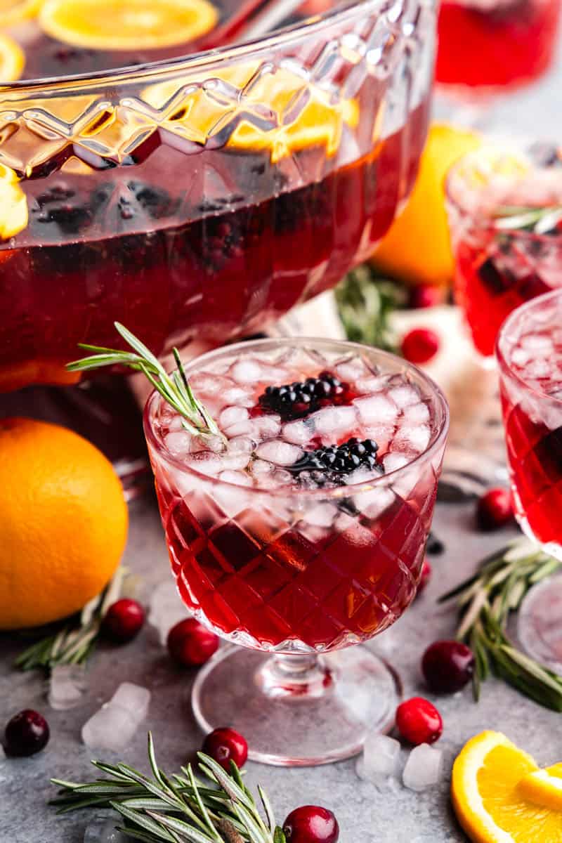 A crystal glass filled with holiday punch set next to a punch bowl and other glasses.