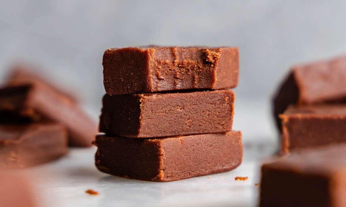 A stack of 3 pieces of old fashioned homemade fudge. The top piece has a bite taken out of it.