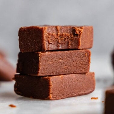 A stack of 3 pieces of old fashioned homemade fudge. The top piece has a bite taken out of it.