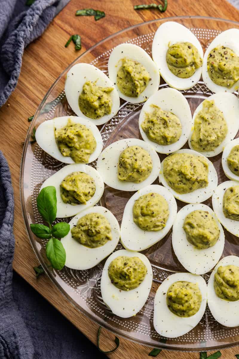 A plate filled with pesto deviled eggs for serving, with a fresh sprig of basil.