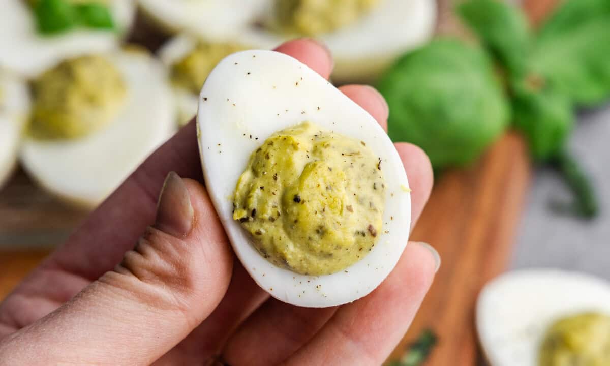 A hand holding up a pesto deviled egg for a close up.