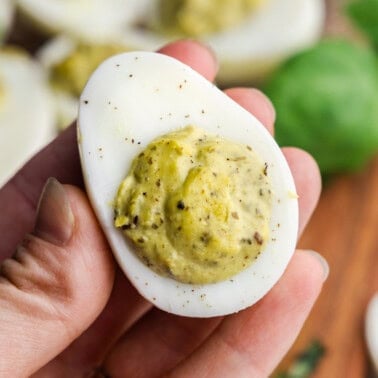 A hand holding up a pesto deviled egg for a close up.