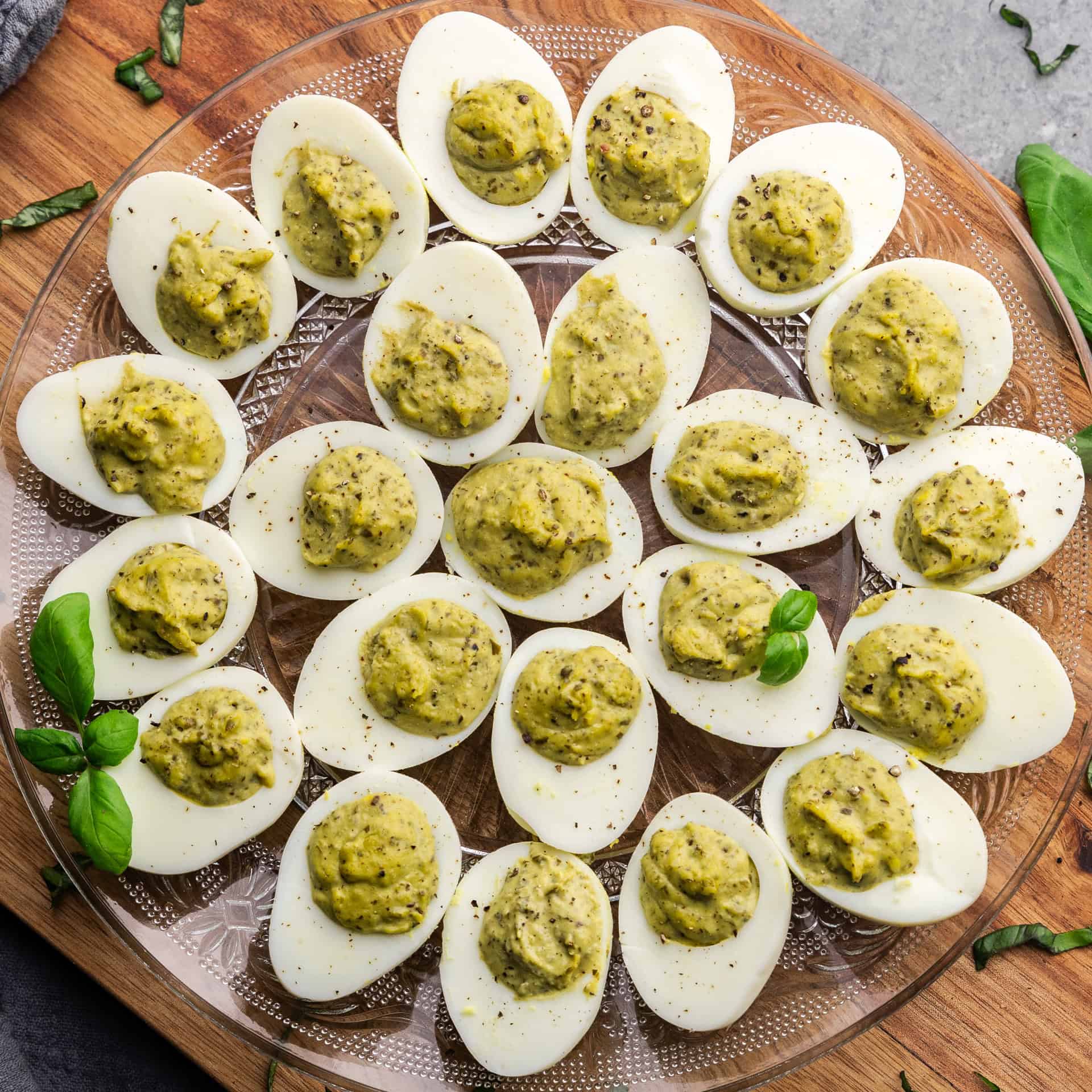 An overhead view of a serving plate filled with pesto deviled eggs set on a wood cutting board.