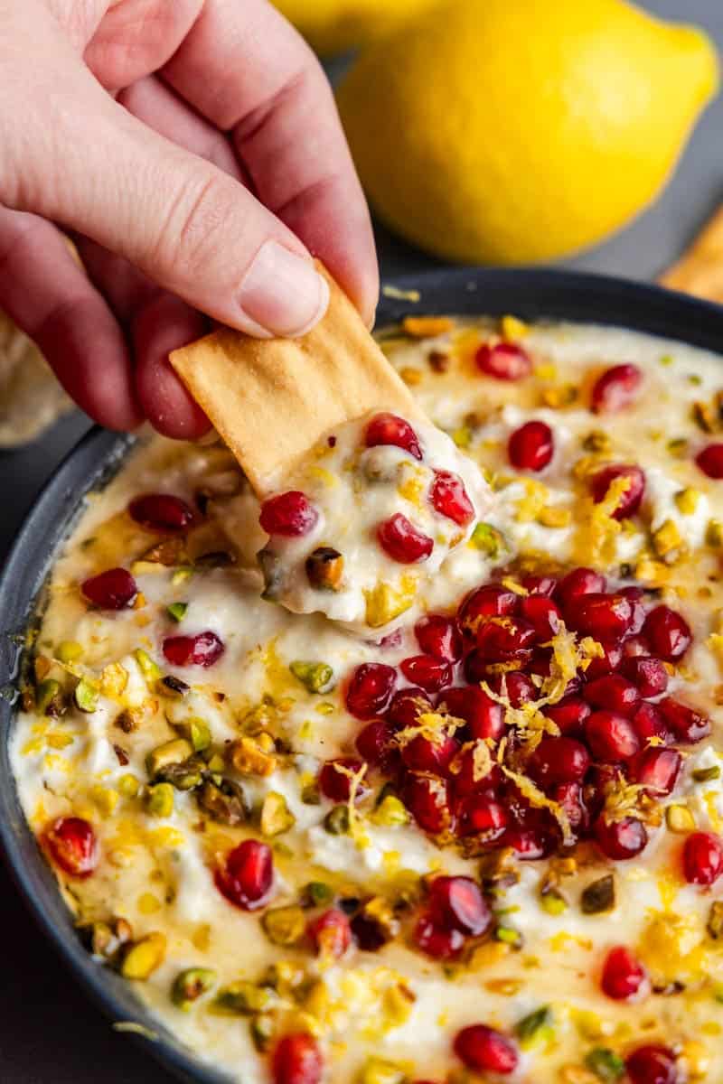 hand dipping pita chip in pomegranate pistachio whipped feta