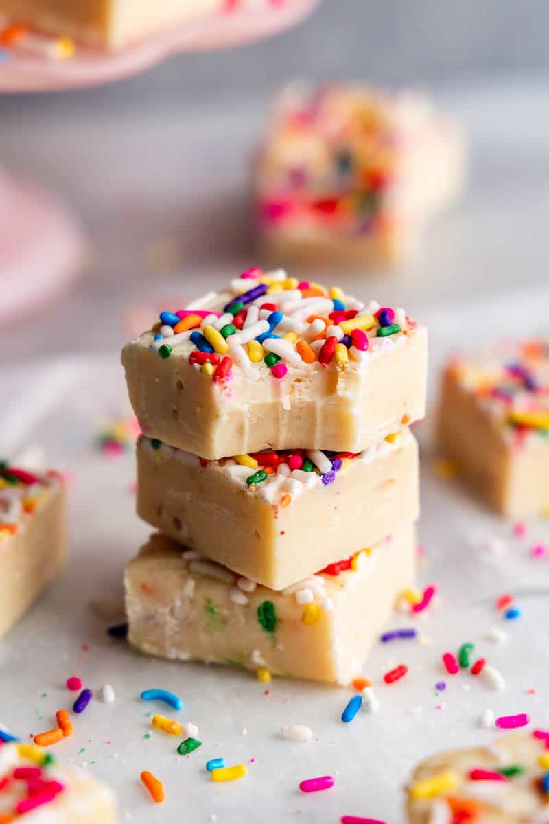 a stack of 3 pieces of homemade sugar cookie fudge. The top piece has a bite taken out of it. 