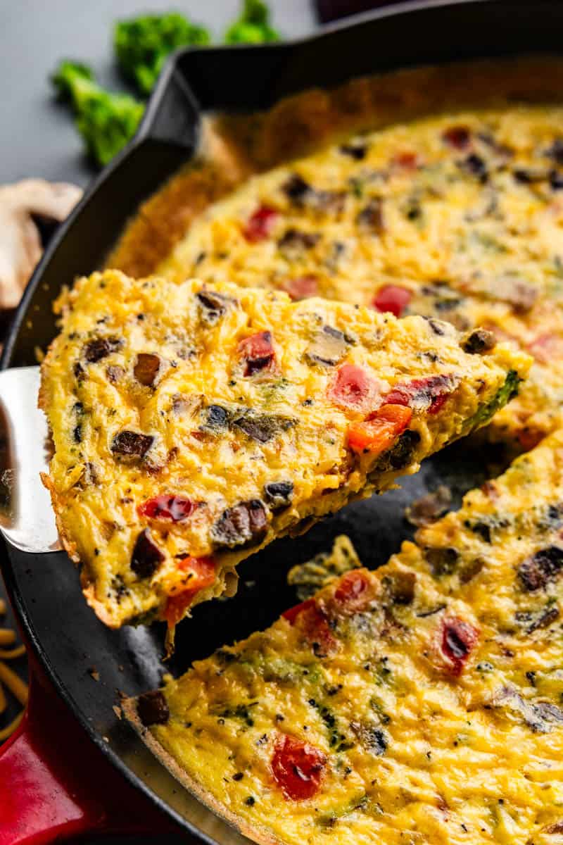 A slice of veggie frittata being lifted out of a cast iron pan.