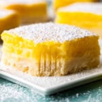 A close up view of a lemon bar on a white plate with a bite taken out.