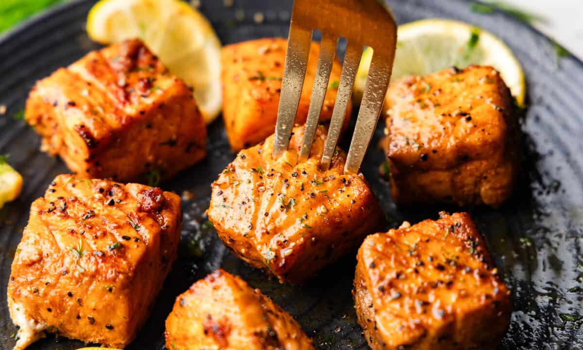 A close up view of air fried salmon bites on a plate with a fork about to lift one up.