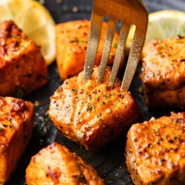 A close up view of air fried salmon bites on a plate with a fork about to lift one up.