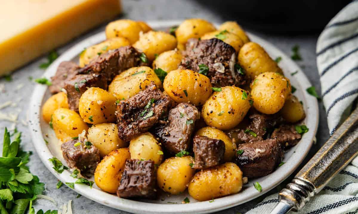 A plate of steak bites and gnocchi garnished with chopped parsley.