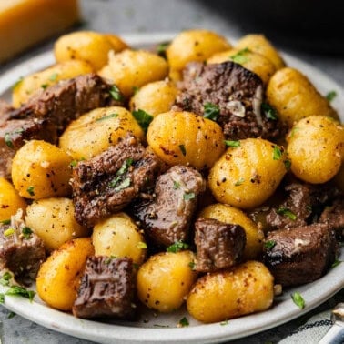 A plate of steak bites and gnocchi garnished with chopped parsley.