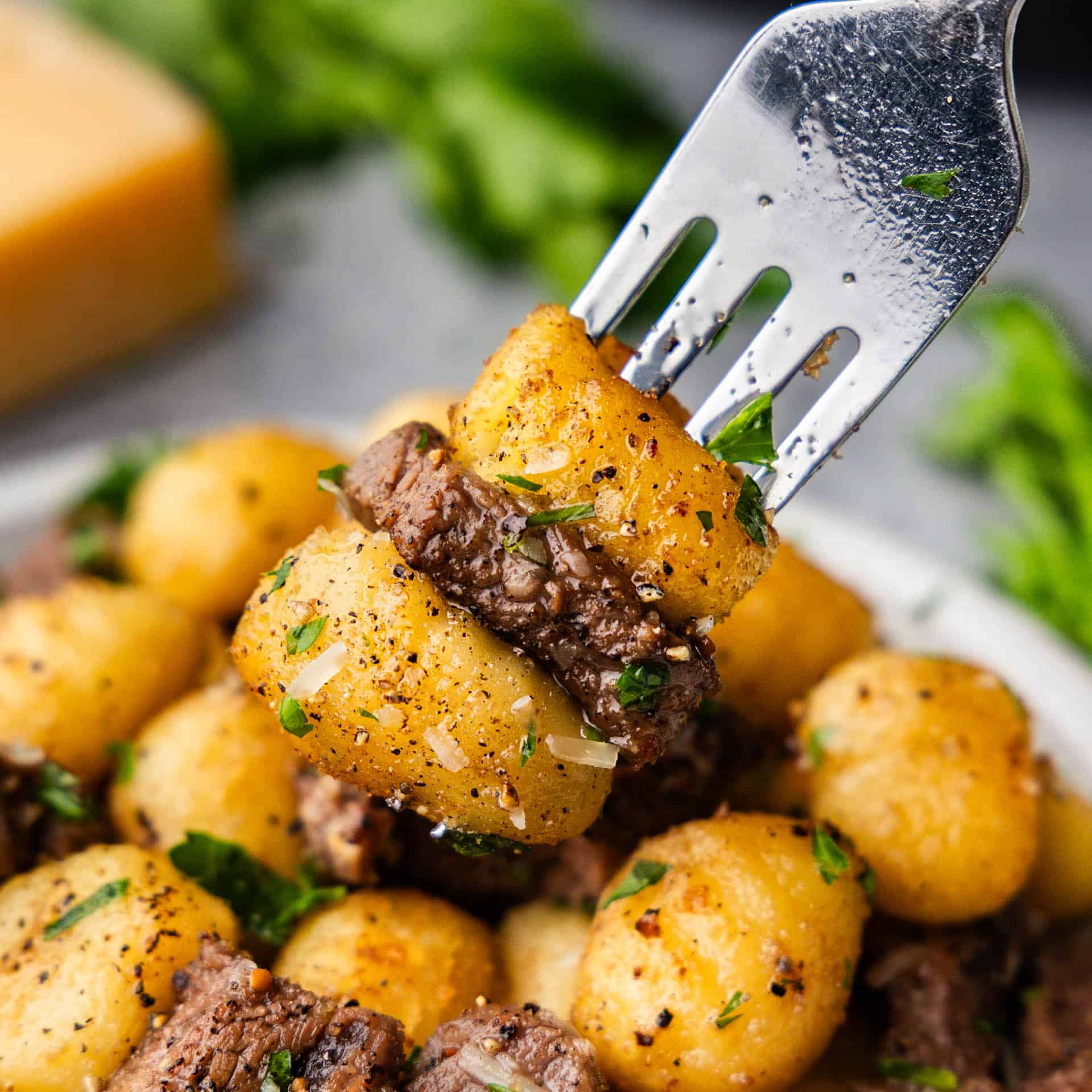 A close up view of a fork lifting a bite of steak bites and gnocchi from the plate.