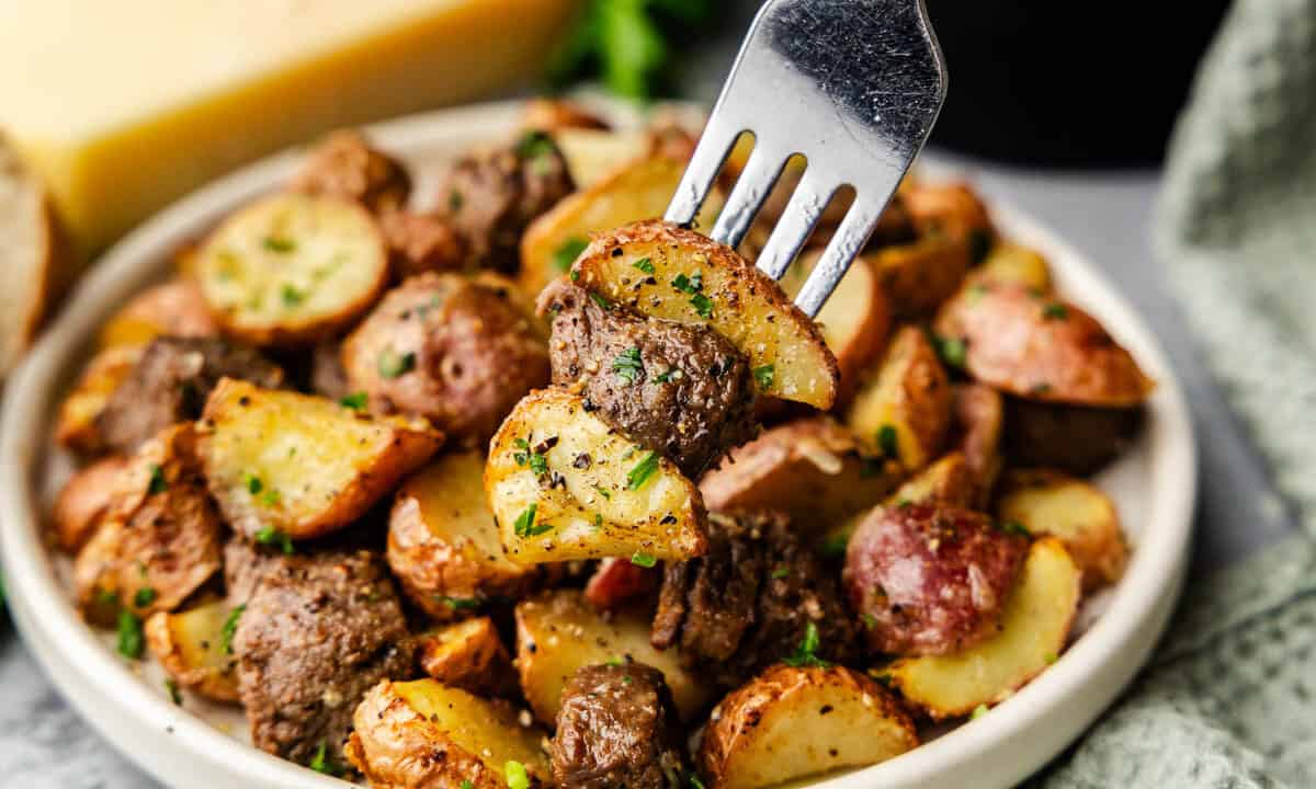 A close up view of a fork lifting a bite of steak bites and potatoes from the plate.