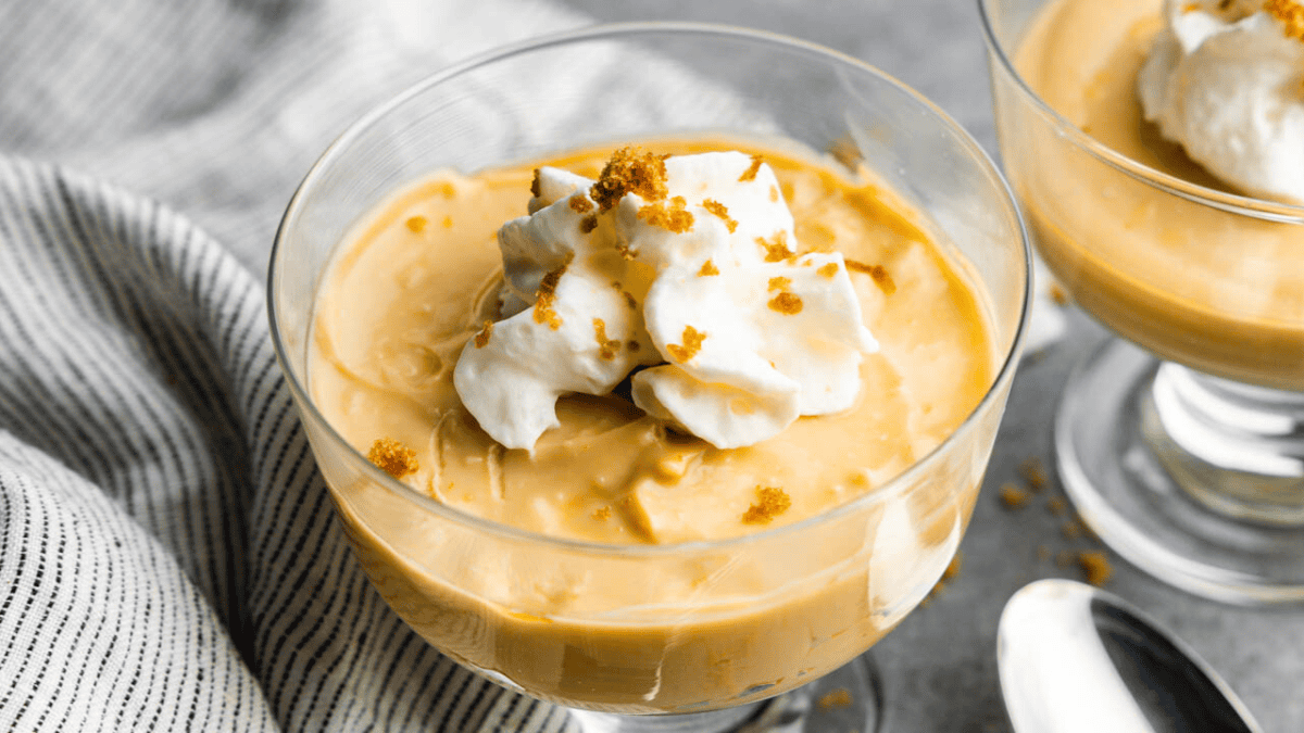 An individual serving glass of butterscotch pudding with a dollop of whipped cream on top.