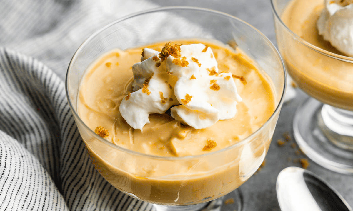 An individual serving glass of butterscotch pudding with a dollop of whipped cream on top.