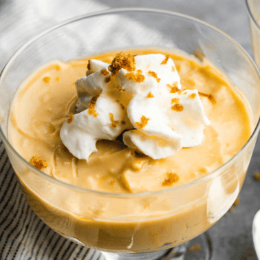 An individual serving glass of butterscotch pudding with a dollop of whipped cream on top.