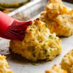 A close up view of a cheddar bay biscuit being brushed with melted butter.