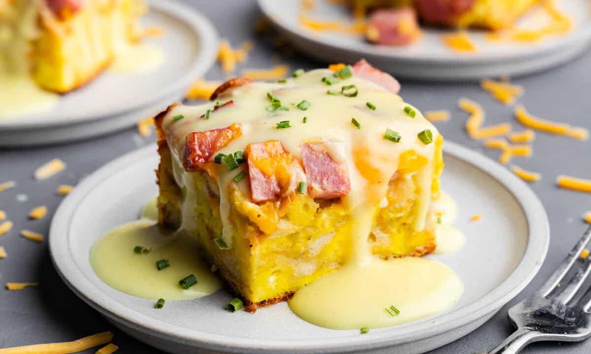 A slice of eggs benedict casserole on a plate with hollandaise sauce drizzled over top.