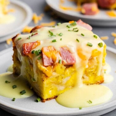 A slice of eggs benedict casserole on a plate with hollandaise sauce drizzled over top.