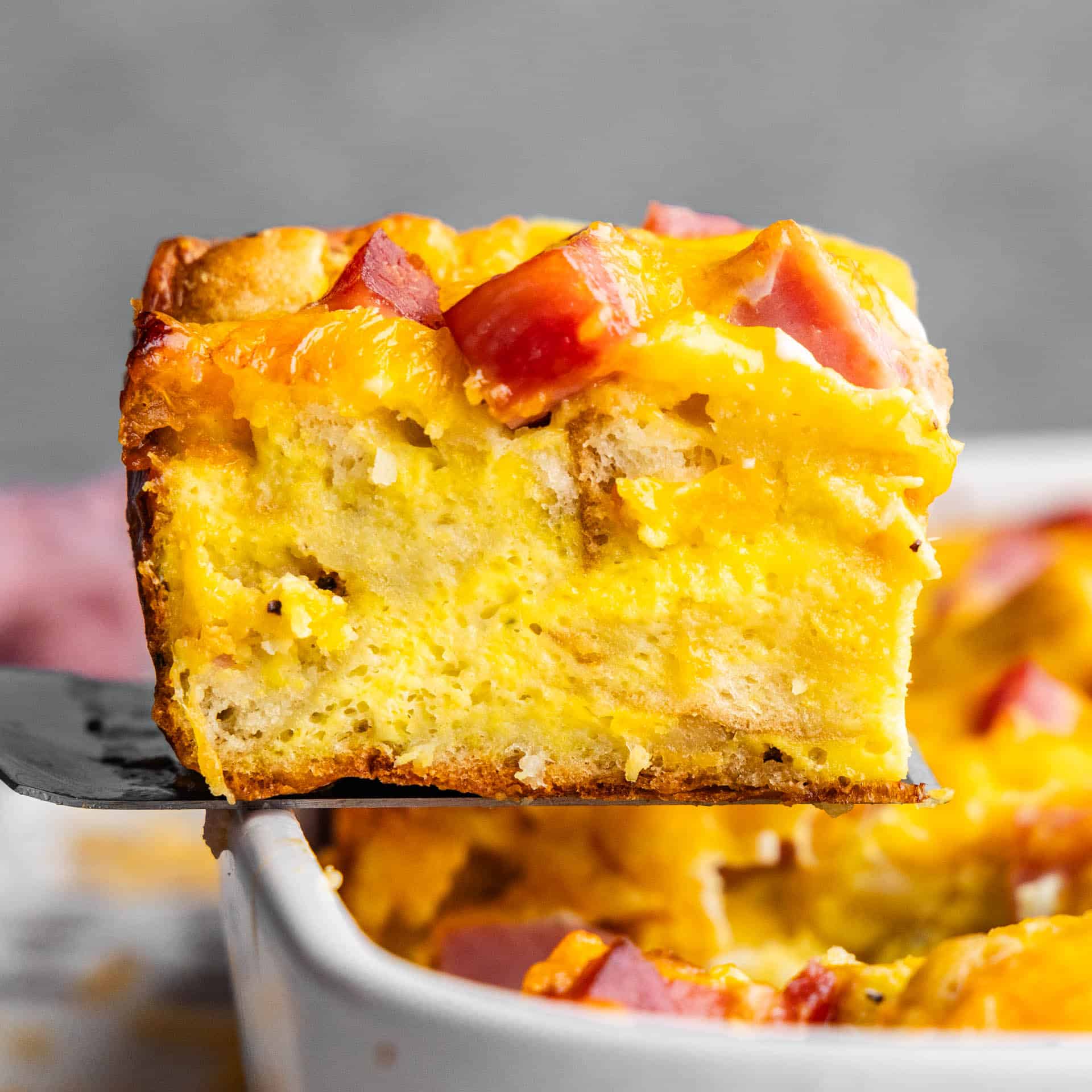 A slice of eggs benedict casserole being lifted from the pan.