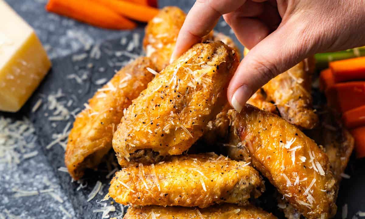 A platter of garlic parmesan chicken wings with a hand pulling one from the pile.