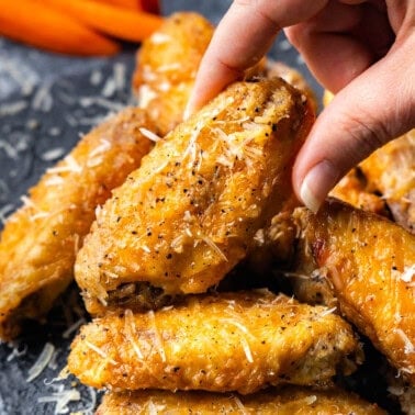 A platter of garlic parmesan chicken wings with a hand pulling one from the pile.