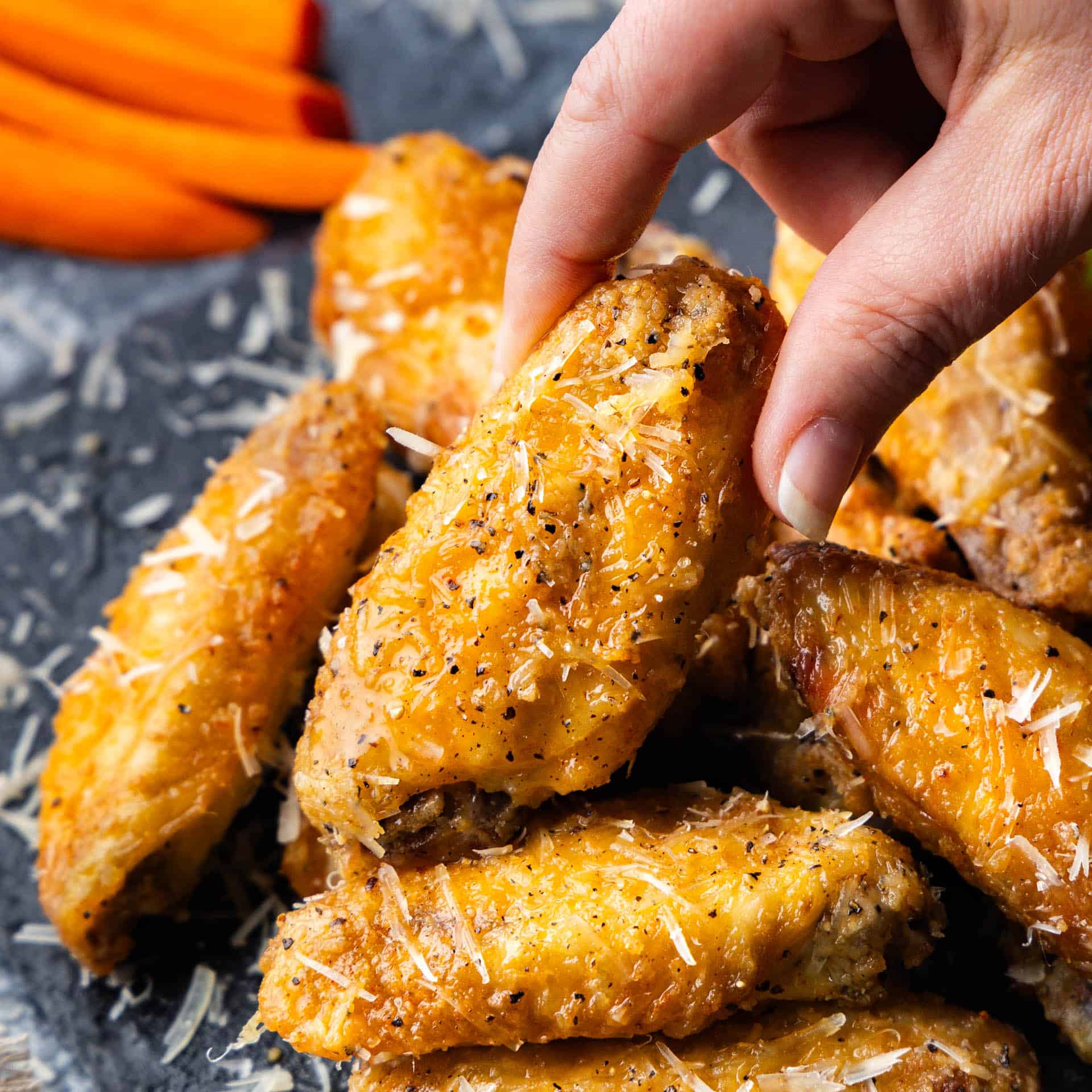 A platter of garlic parmesan chicken wings with a hand lifting a piece from the pile.