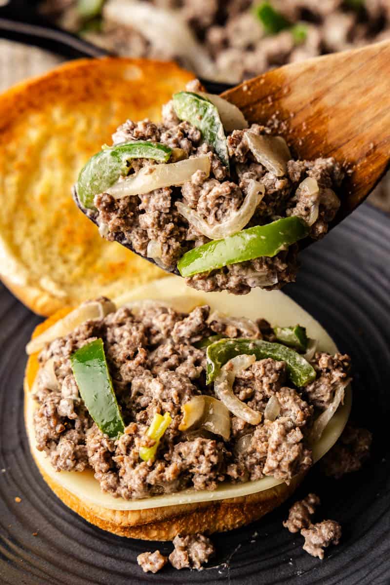 a wooden spoon scooping cheesesteak sloppy joes onto bun