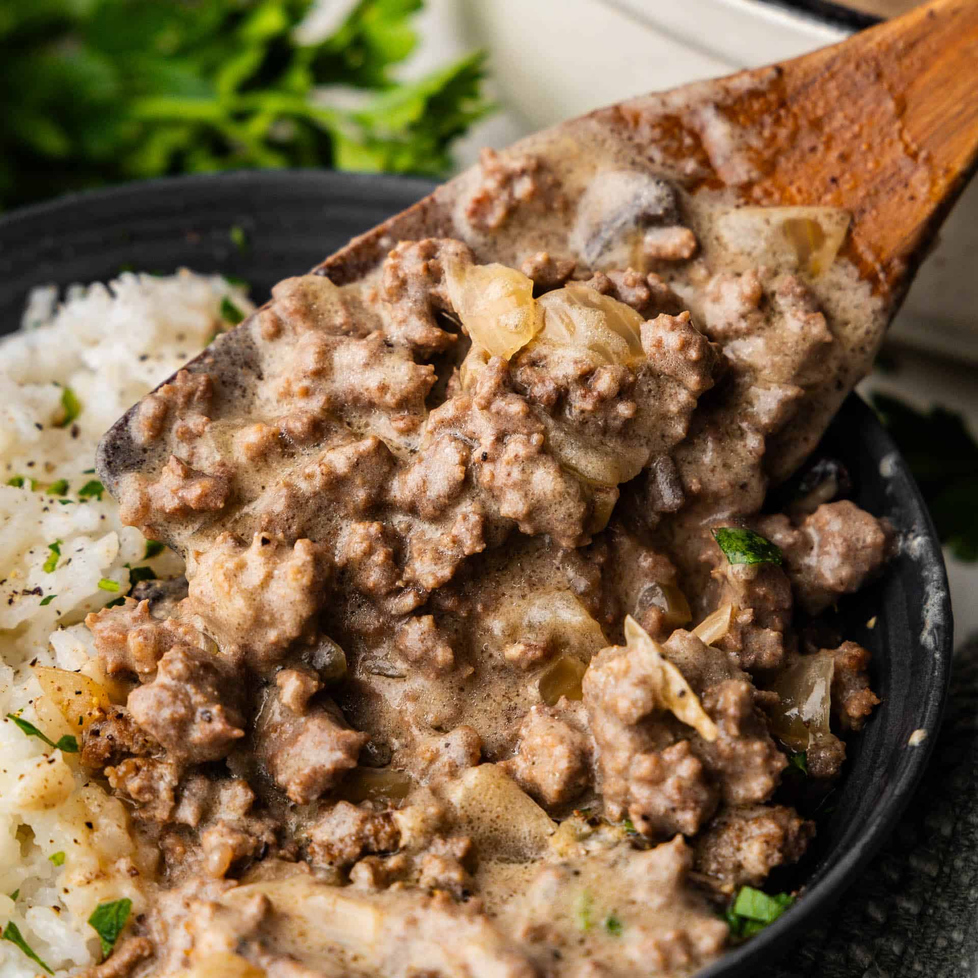 A wooden spoon dishing out a helping of ground beef stroganoff to serve over white rice.