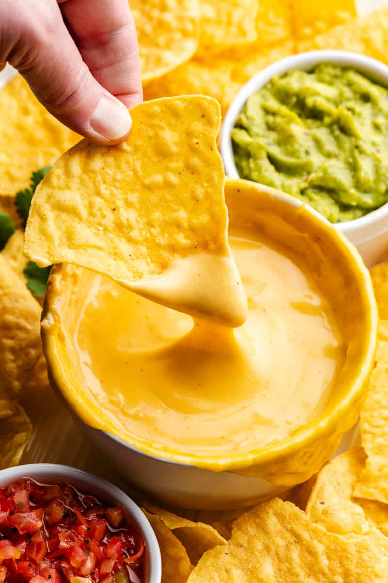 hand dipping chip into bowl of homemade nacho cheese sauce