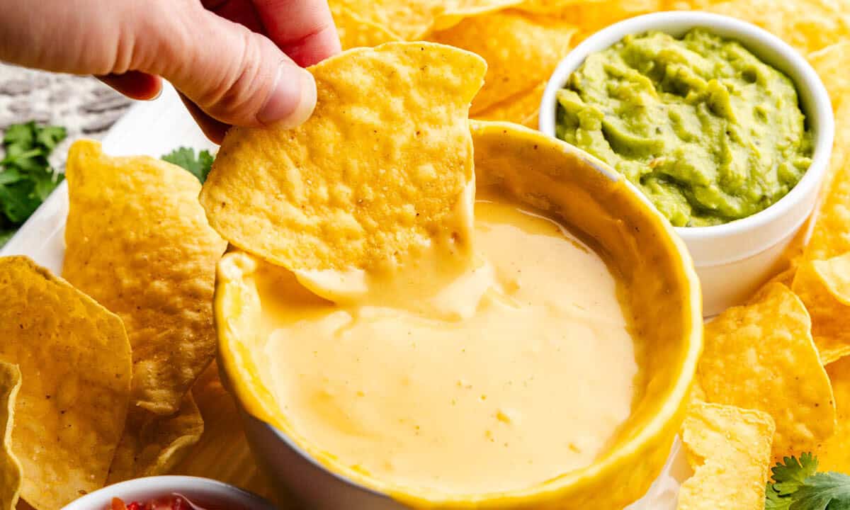 chip being dipped in bowl of homemade nacho cheese sauce