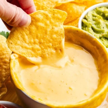 chip being dipped in bowl of homemade nacho cheese sauce