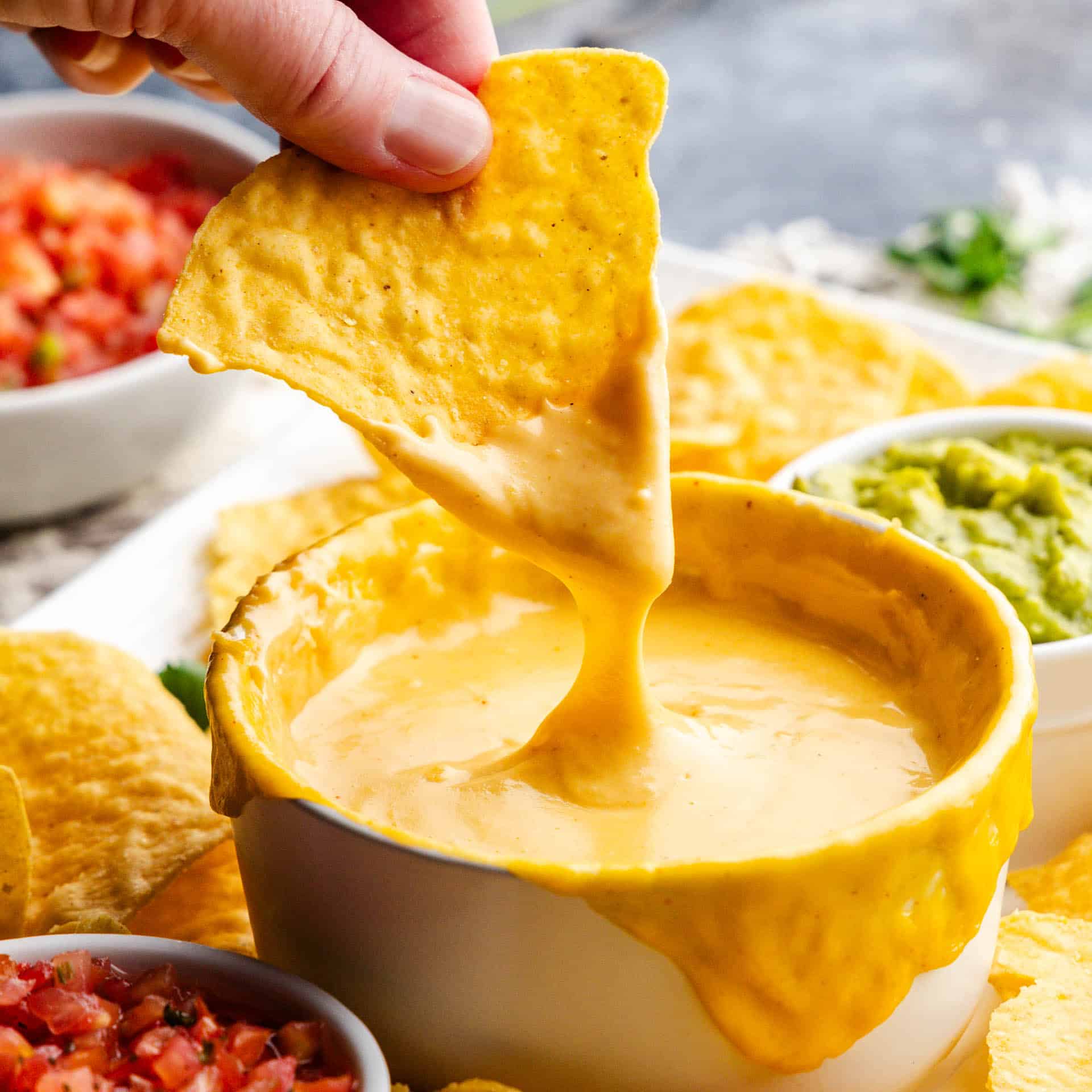 hand dipping chip in bowl of homemade nacho cheese sauce