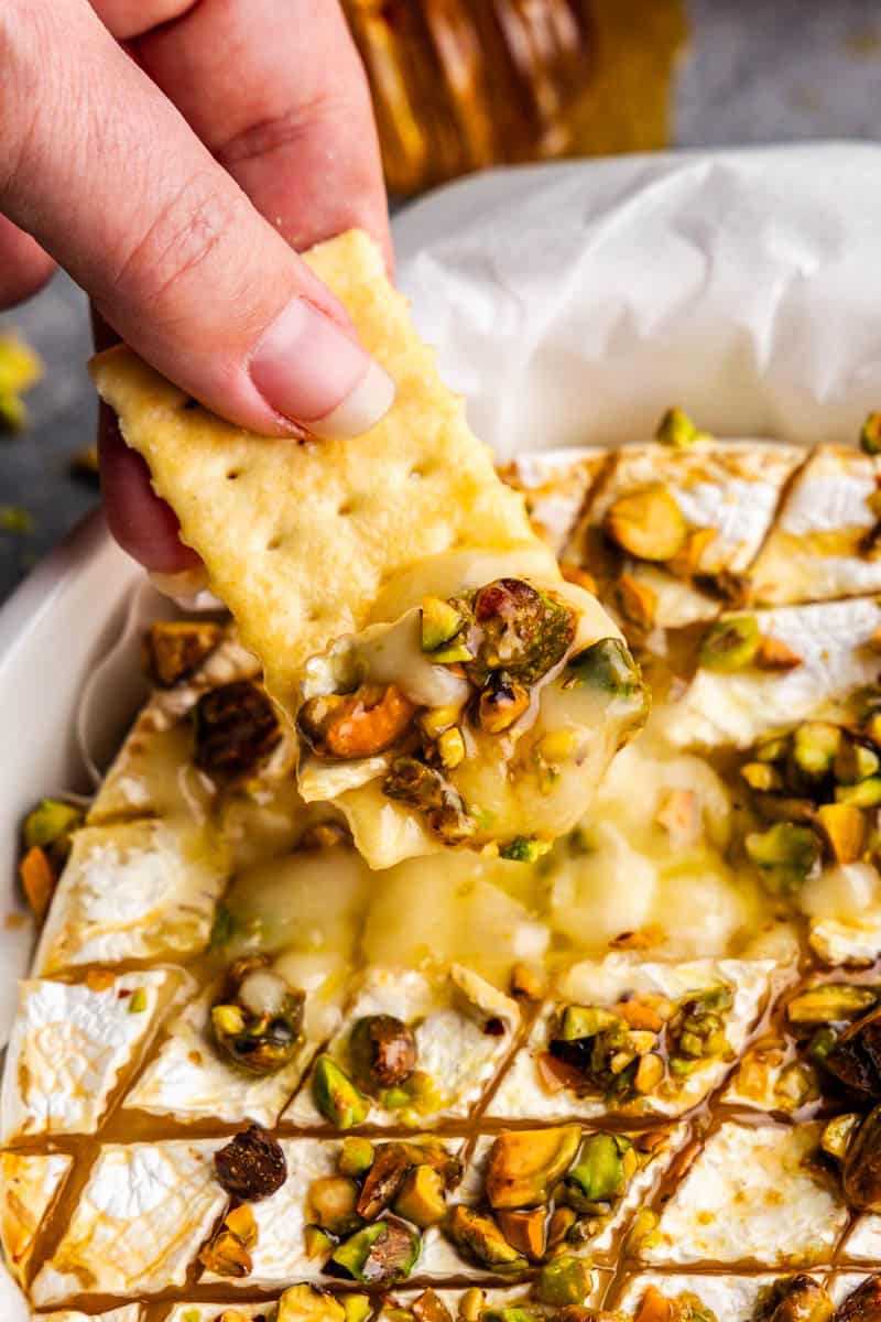 A close up view of a cracker being dipped into hot honey pistachio baked brie.