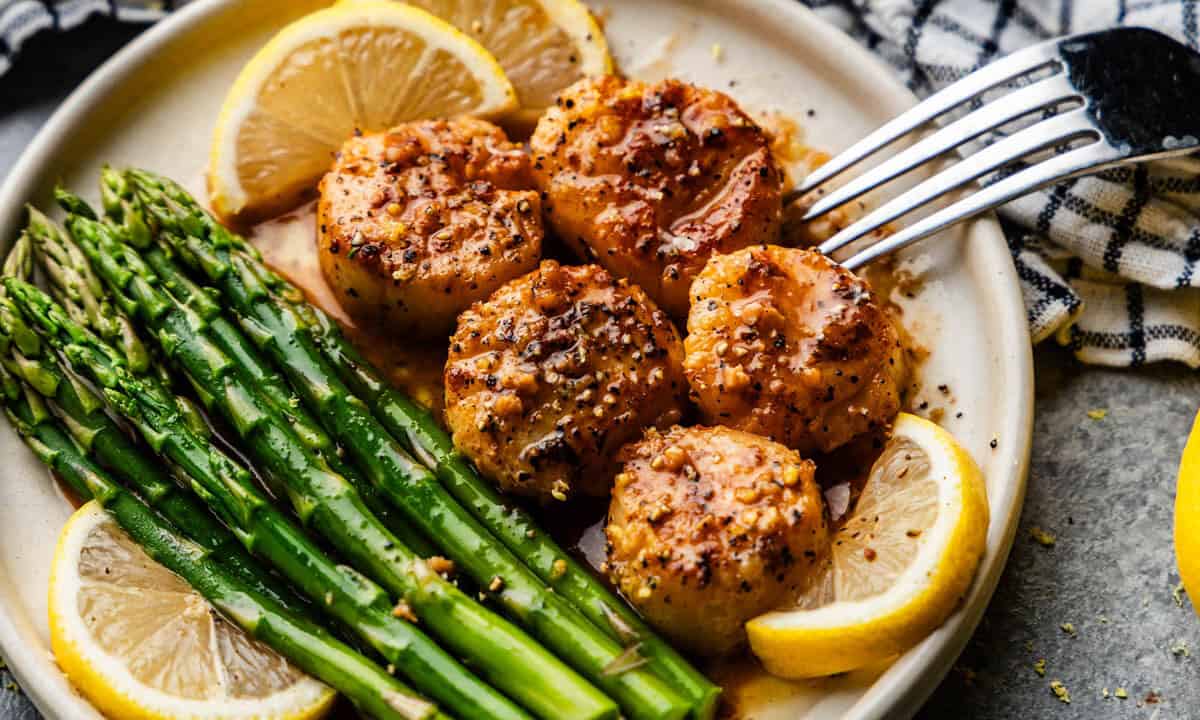 A plate of scallops with lemon slices and asparagus on the side.