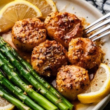 A plate of scallops with lemon slices and asparagus on the side.