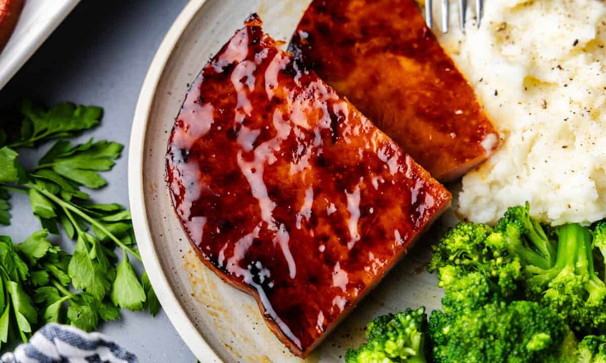 slice of maple and mustard glazed ham steak on plate with broccoli and mashed potatoes